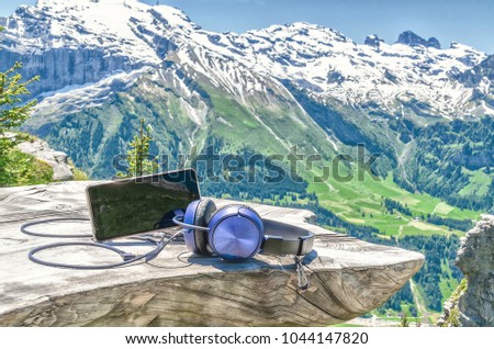 cell phone with headphones on a wooden table on the background of the Swiss Alps and mountain scenery.
