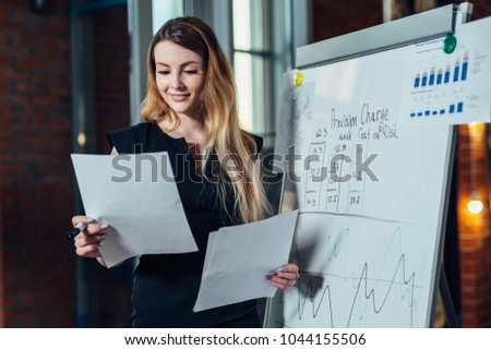 Female office worker working on her presentation standing near white board reading the report printed on paper Royalty-Free Stock Photo #1044155506
