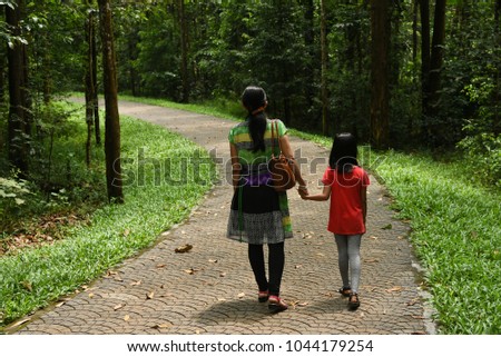 Mother and child walking, relaxing in natural green forest walkway. Having fun with family in Kerala, India.