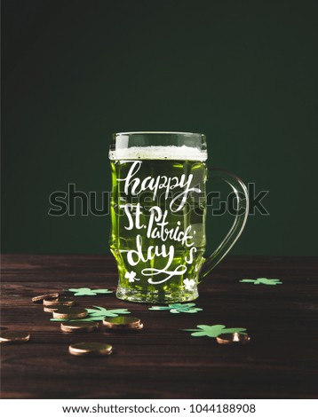 close up view of glass of beer on wooden tabletop and happy st patricks day lettering