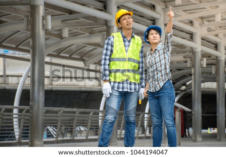 Picture of professional Asian engineering team wearing safety helmet talking about construction project and pointing finger up at construction site