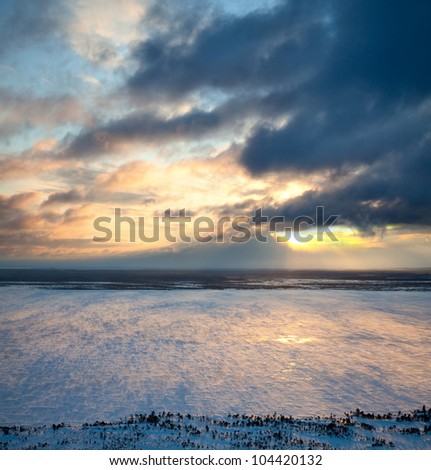 Aerial view of winter landscape with frozen lake on the background of a windy sunset.