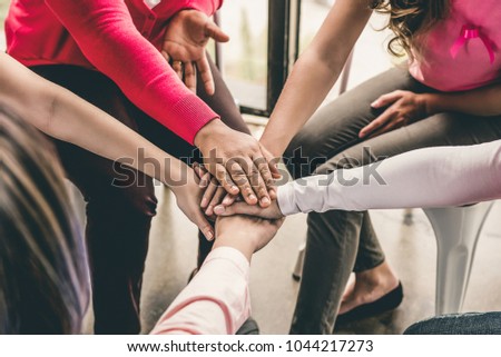 Group of diverse women put their hands together in stack empowering each other in breast cancer awareness campaign meeting Royalty-Free Stock Photo #1044217273