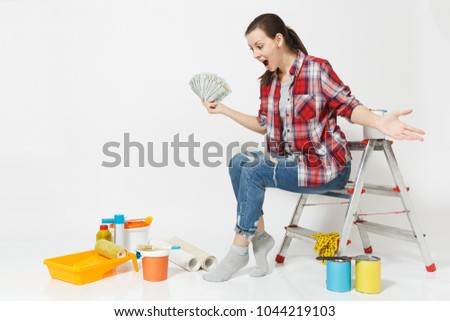 Woman holds bundle of dollars, cash money, sits on ladder with instruments for renovation apartment isolated on white background. Wallpaper accessories for gluing painting tools. Repair home concept