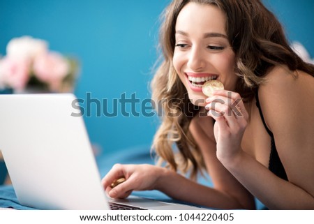 Young and happy woman buying online with cryptocurrency concept, woman holding golden crypto coin lying with laptop on the bed at home Royalty-Free Stock Photo #1044220405