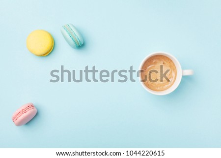 Cozy morning breakfast. Cup of coffee and colorful macaron on pastel blue background top view. Fashion flat lay style. Sweet macaroons.