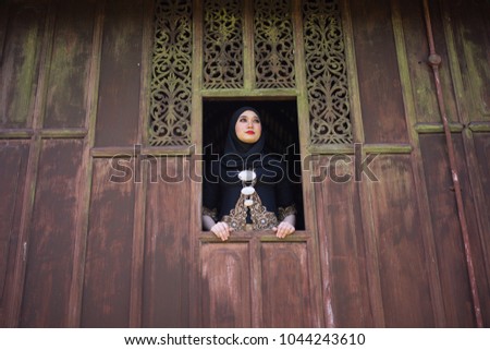 Fashion portraiture of young beautiful malay woman wearing modern kebaya looking out of the window of traditional house.