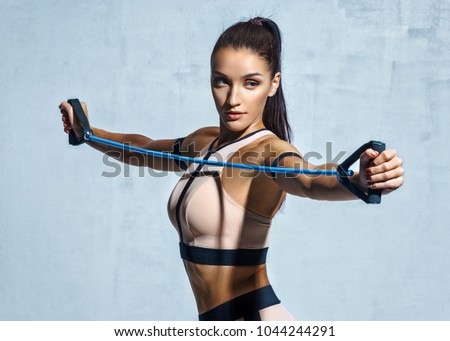 Athletic girl performs exercises using a resistance band. Photo of young girl on drey background. Strength and motivation