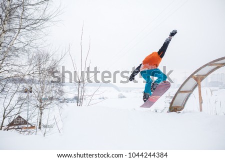 Photo from back of young athlete skating on snowboard with springboard against background of trees