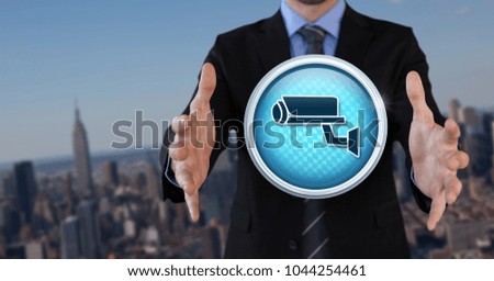 Digital composite of Security camera icon and Businessman with hands palm open in city