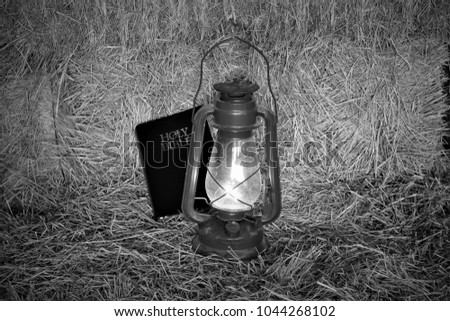 Black and white picture of a bible on a bale of hay with light from  an oil lantern.