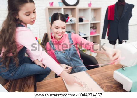 Mom and daughter work together in a sewing workshop. The girl is holding the thread. There is a sewing machine on the table.
