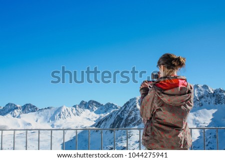 Girl taking picture of snowy mountain peaks in ski resort.