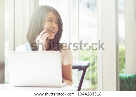 Portrait of cute asian teen woman talking smartphone and a laptops or notebook computer in coffee cafe. morning or sunset moment. filtered image and light effect added. happy smile chill out concept