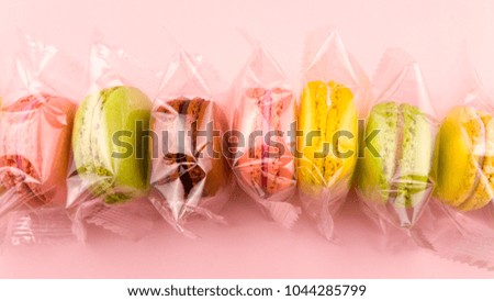 Color macaroons or macaron in transparent package on pastel pink background.