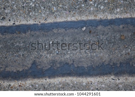 Close up outdoor view from above of a small concrete drainage canal. Colored water traces drawing lines on the curved surface. Textured structure. Abstract urban picture taken near a pathway in France