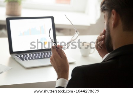 Tired of computer work businessman taking off glasses feeling eyestrain in front of laptop, employee having bad eyesight vision problem, eyes fatigue and overwork concept, rear over the shoulder view Royalty-Free Stock Photo #1044298699