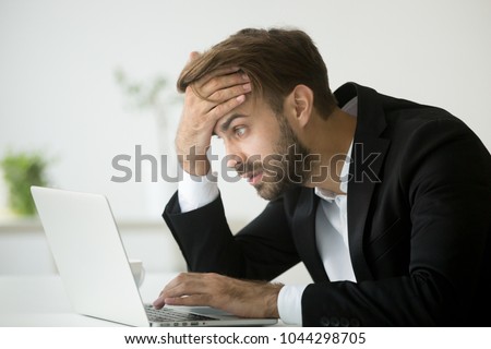Worried stressed businessman in suit shocked by bad news using laptop at work, desperate bankrupt investor lost money online depressed by financial problem debt, frustrated worker tired of overwork Royalty-Free Stock Photo #1044298705