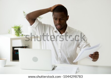 Confused african-american businessman having problem with documents looking at laptop at work, frustrated black employee stressed by mistake or unexpected computer error crash, forgot about deadline Royalty-Free Stock Photo #1044298783
