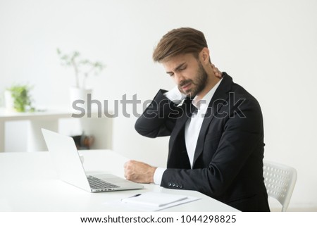 Young businessman in suit feels neck pain massaging tensed muscles after sedentary work sitting on uncomfortable office chair, employee having computer syndrome suffers from chronic cervicalgia ache Royalty-Free Stock Photo #1044298825