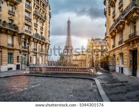 small paris street with view on the famous paris eiffel tower on a cloudy rainy day with some sunshine Royalty-Free Stock Photo #1044301576