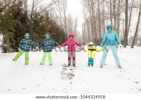 Happy young mother in blue ski suit wearing sunglasses with funny children in bright winter clothes, walking holding hands in park. Wonderful winter holidays for whole family. Children fun together