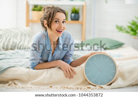Portrait of a beautiful woman lying with alarm clock in the cozy and bright bedroom at home