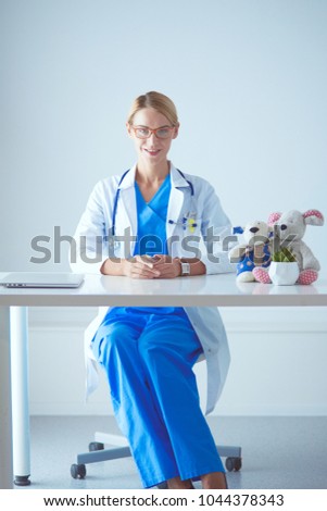 Beautiful young smiling female doctor sitting at the desk.