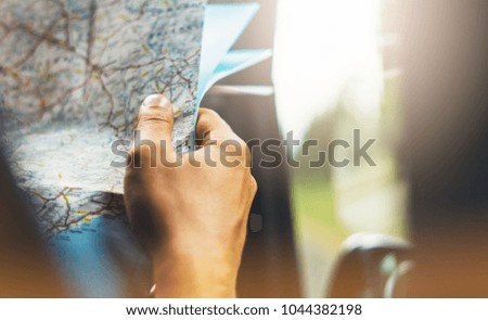 Hipster man holding in male hands and looking on navigation map in auto, tourist traveler hiker driving on background panoramic view way road, trip in transportation, person sitting on backdrop window