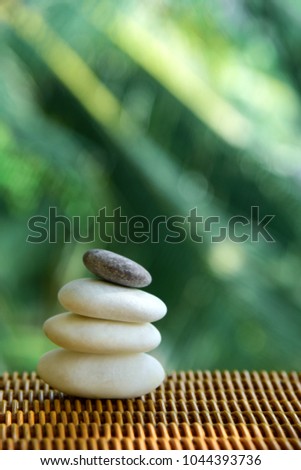 Zen stones on a rattan table. Emerald-green tropical  background.