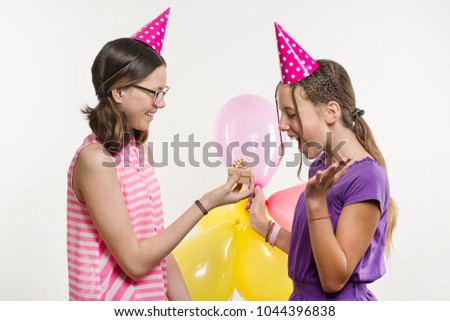 Birthday party. Girls teenagers give a gift. White background, in festive hats with balloons.