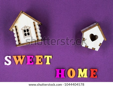 The phrase "Sweet home" laid out on a pink background with two toy wooden houses.