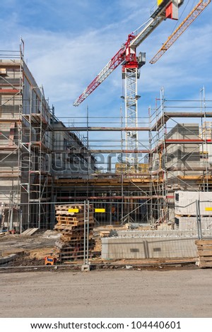 Large construction site with scaffolding building, yellow tower crane and clear blue sky.