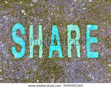 The word SHARE stencilled in turquoise and green letters onto the floor made out of wet pour rubber surface material in a kids playground with space for copy. Mitcham, England