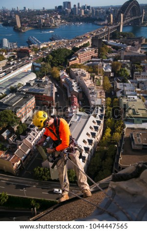 Construction rope access worker wearing yellow hard hat, long sleeve shirt safety harness, and a white bucket, working, abseiling off from the high rise building at circular quay, Sydney, Australia