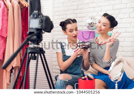 Two fashion blogger girls in jeans and shirt with skirt hold up eye shadows and brushes to camera.