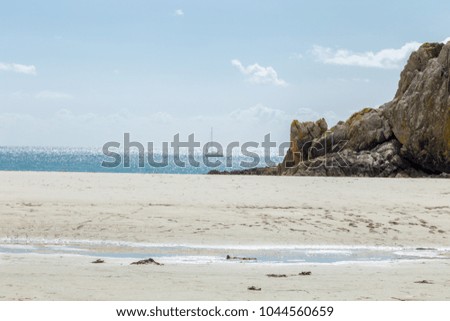 Sea beach with huge stone rocks and sail boat contrasting the sand