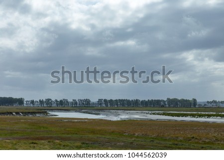 French european estuary with trees and a green field. Gray day.