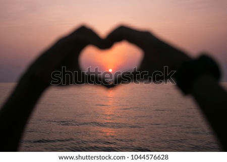 Blurred hand love heart sign at the sunset background by the sea   