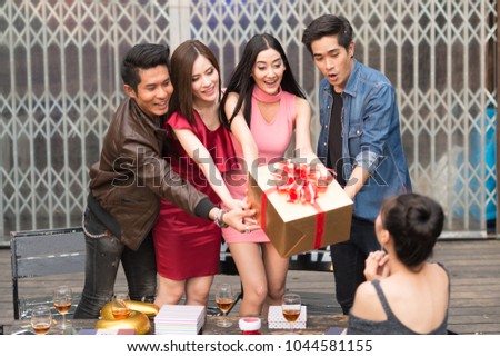 Friends celebrating birthday and giving gift to a girl sitting in a dining room. Birthday or New Year eve celebrating concept