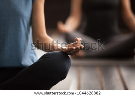 Sporty woman in blue t-shirt practicing yoga lesson, sitting in Sukhasana exercise, Easy Seat pose, working out, indoor close up focus on mudra gesture, studio Royalty-Free Stock Photo #1044628882