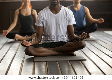 Young black man and a group of sporty people practicing yoga lesson with instructor, sitting in Sukhasana exercise, Easy Seat pose with mudra gesture, working out, indoor close up, studio floor Royalty-Free Stock Photo #1044629401