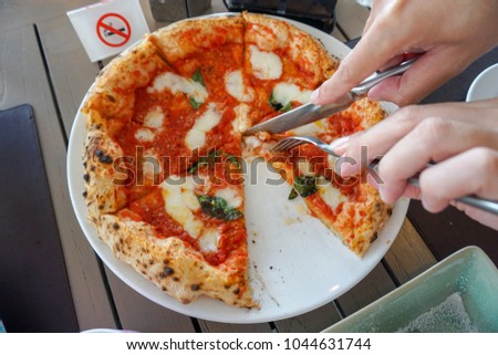 Asian man use a knife and fork eating pizza, Italian classic pizza Margherita on the wooden table. No smoking sign.
