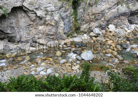 A stream that runs through the middle of the mountains Beside a stream lined with rocks.