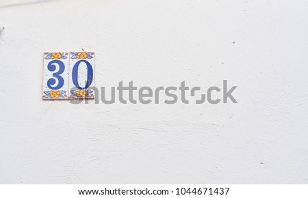 House number on the wall thirty, detail of a wall of a house with a number of information.