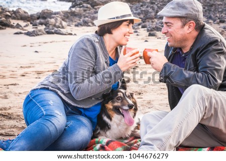family with a border collie dog doing pic nic activity on the beach in vacation, summer lifestyle with friends concept. old style and vintage filter. tea break time