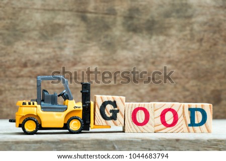 Yellow toy forklift hold letter block G to complete word good on wood background