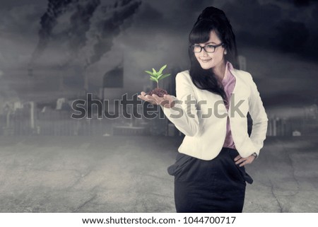 Picture of beautiful business woman holding a plant while standing in the polluted city 