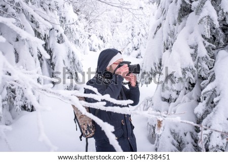 A young man European appearance in glasses with a backpack and a camera in the hands of a winter forest picks up