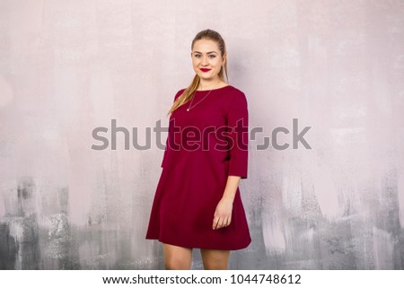 young beautiful girl in a red dress stands on a pink background and smiles
